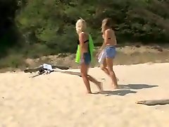Two teenage girls are at the beach. They spread a blanket down on the...